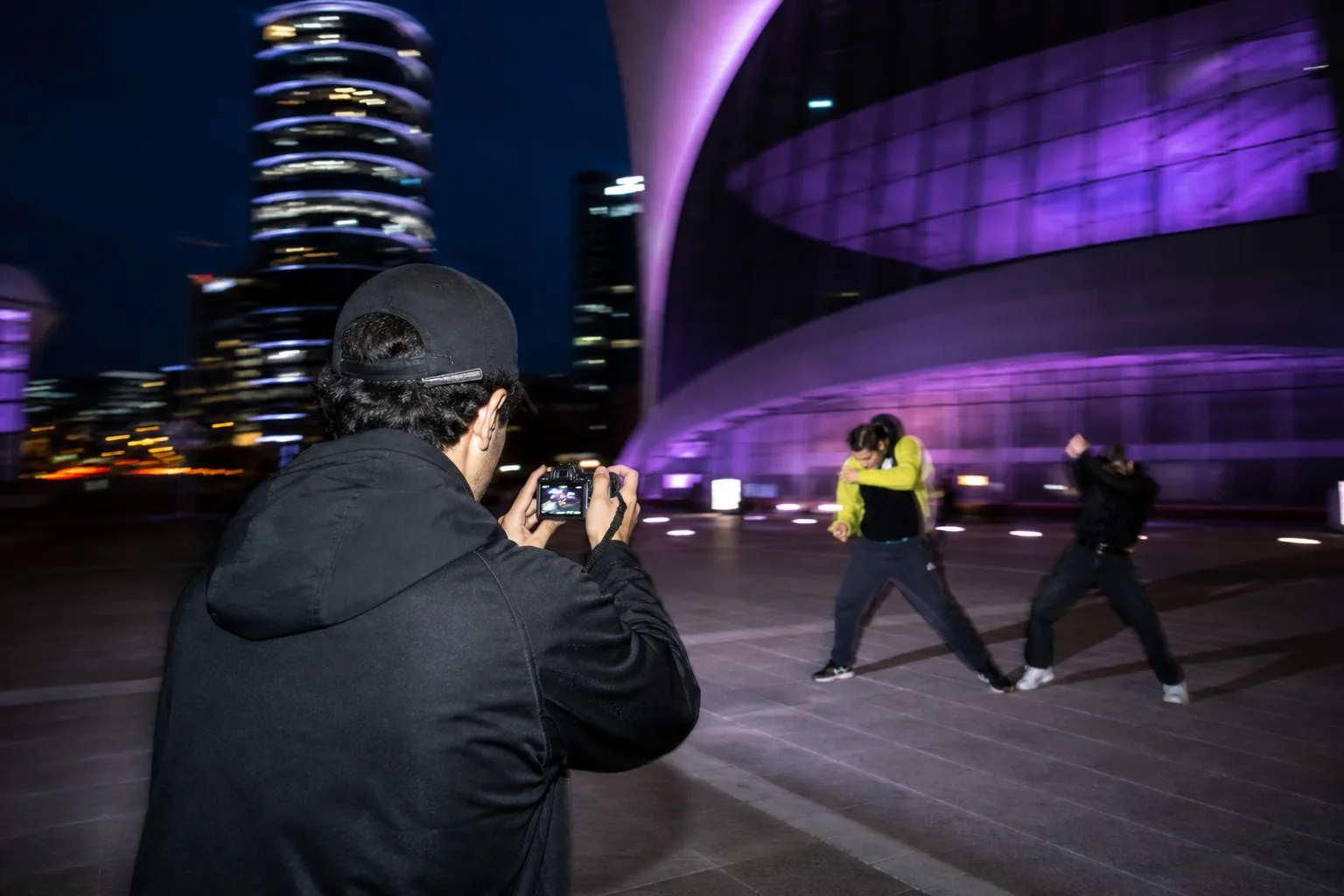 Creator filming in a purple-lit city plaza at dusk.